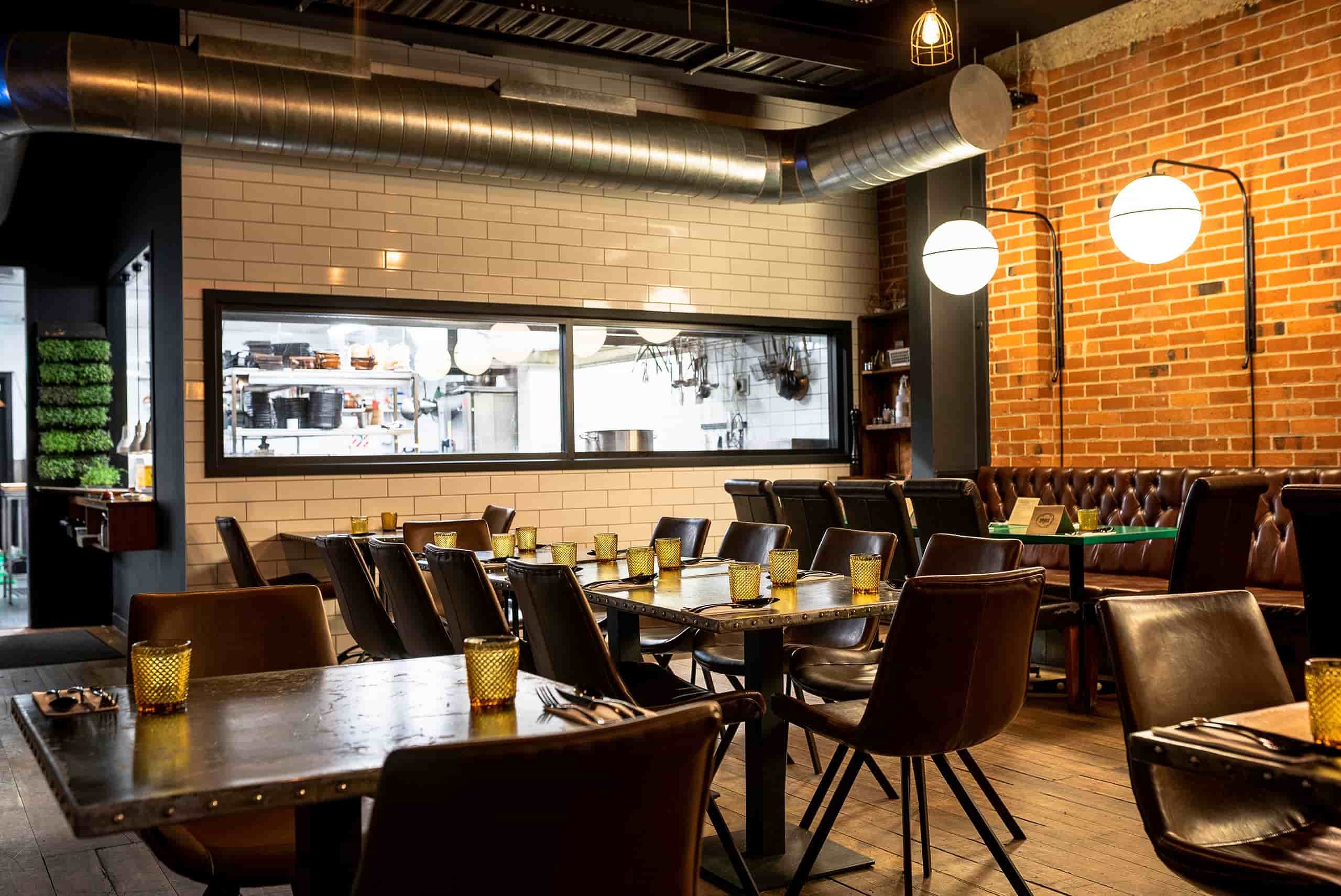 Brick-walled restaurant with dark timber tables, pendant lights, and pass window to kitchen