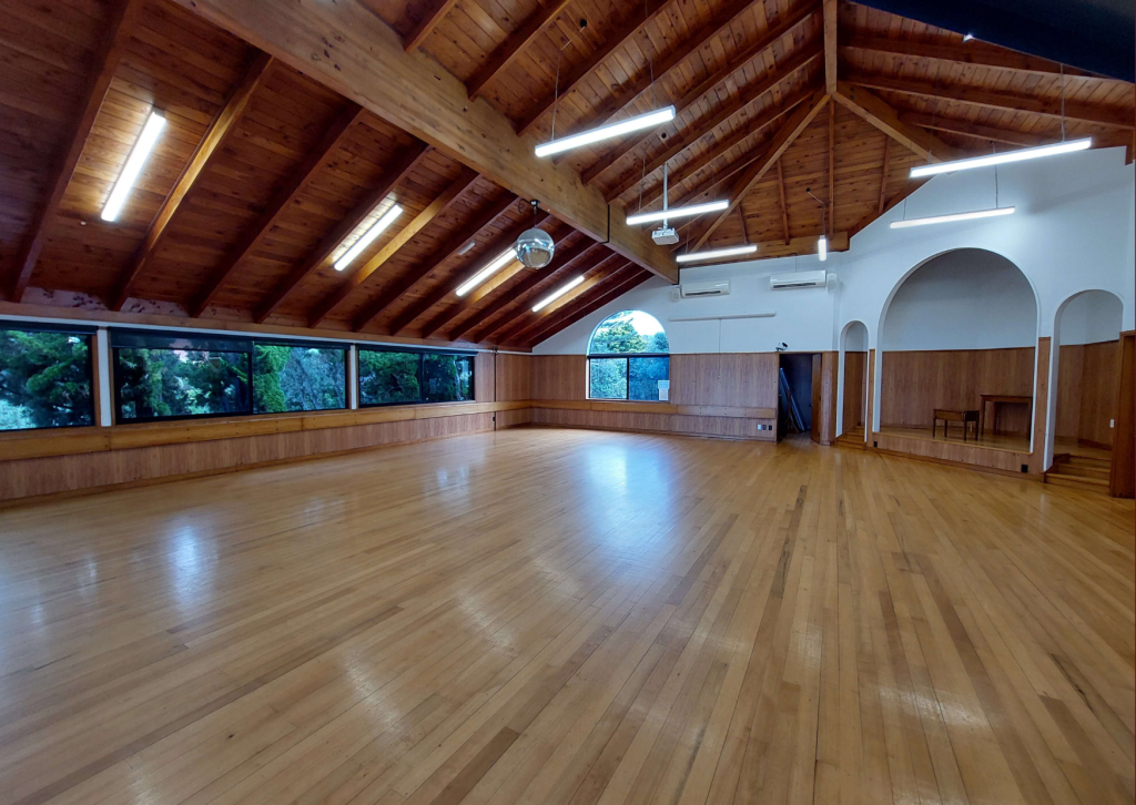 Empty hall with exposed timber roof trusses, polished floor and arched openings