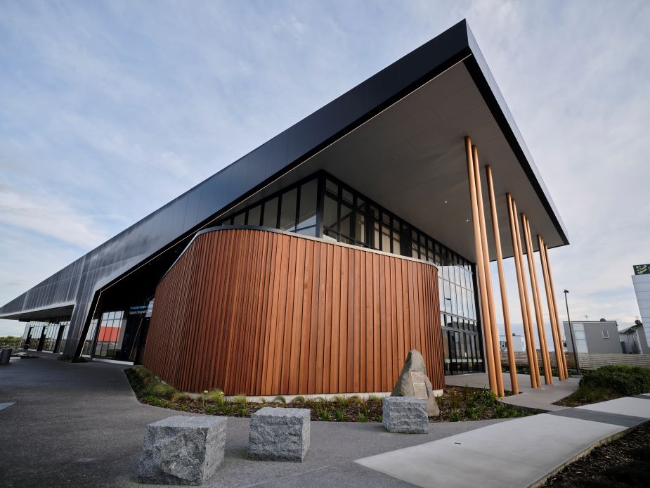 Contemporary building with curved dark timber cladding, metal roof canopy, and tall bronze columns