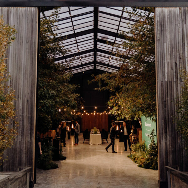 Glass-roofed pavilion interior with trees growing inside, viewed from entrance at night