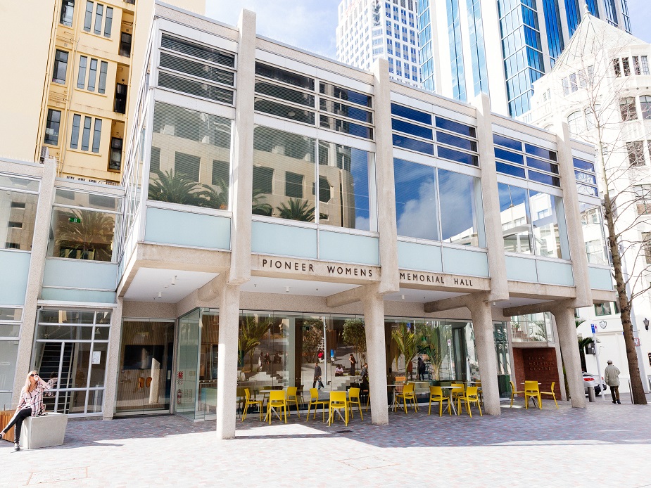 Glass-fronted Pioneer Womens Memorial Hall building on city square with outdoor cafe seating
