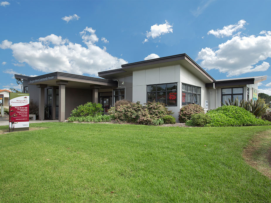 Single-storey community building with flat roof, large windows, and lawn in front