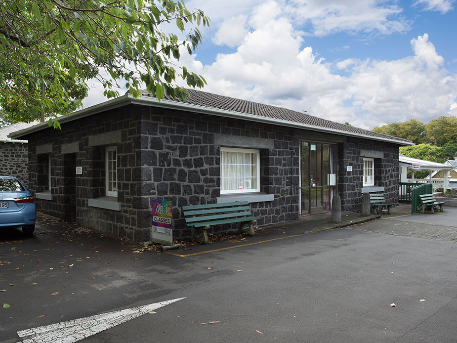 Small dark stone masonry building with bench seating at the entrance