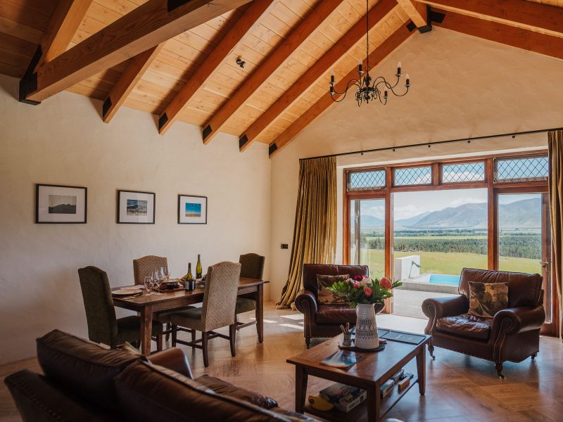 Vaulted timber-beam room with leather sofas, dining table and large window framing mountain panorama