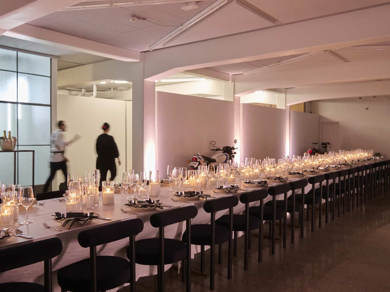 White warehouse interior with long candlelit table, concrete floor, and pink uplighting