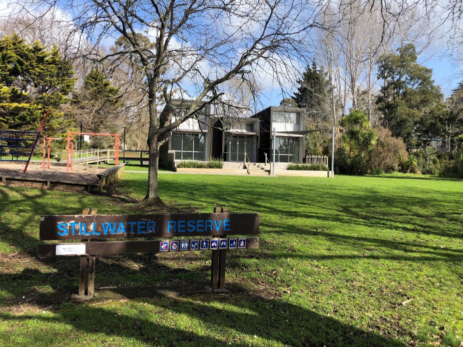 Reserve sign in front of a two-storey dark building with large windows and mature trees behind