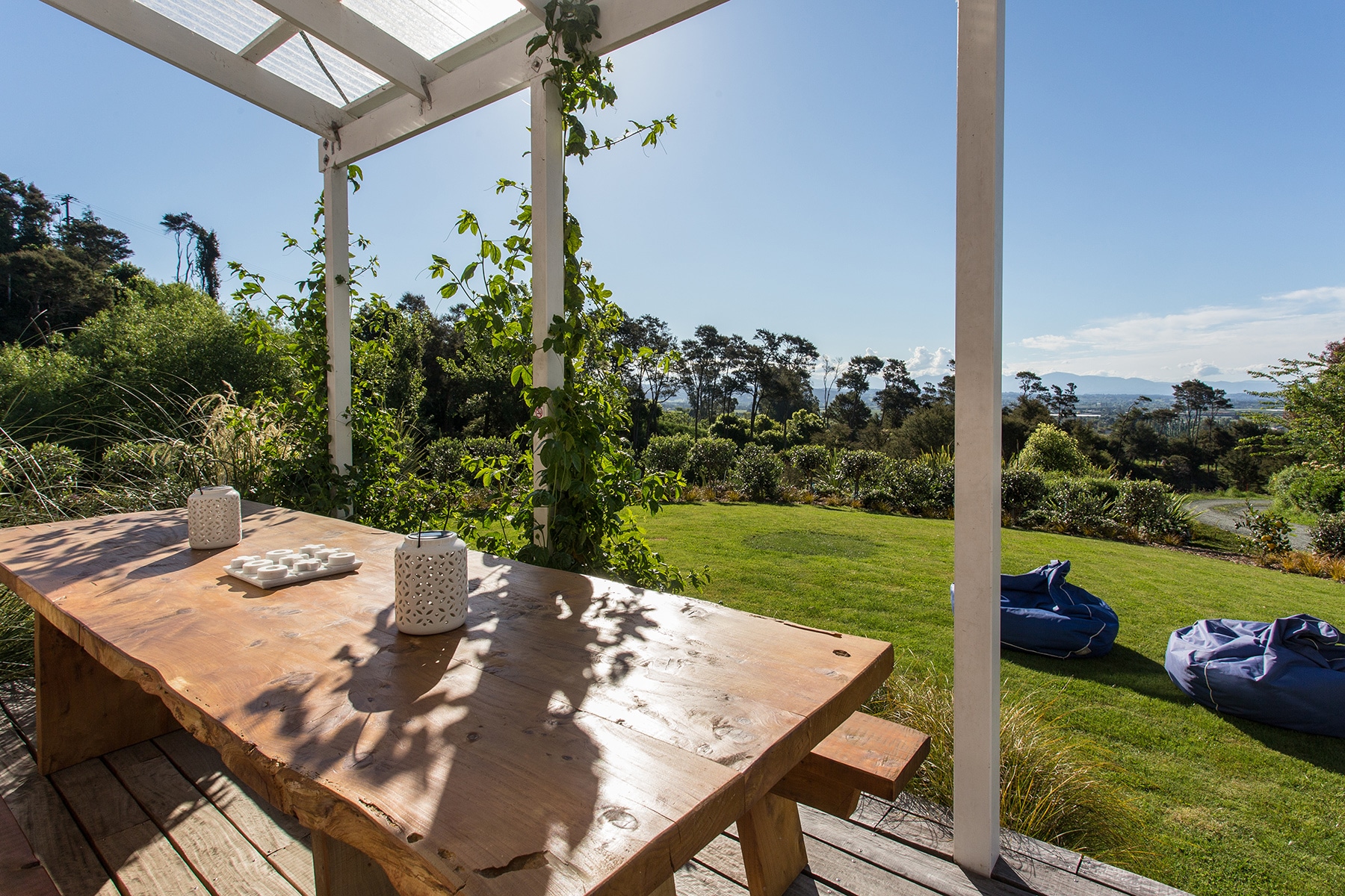 Timber deck with table under white pergola, lawns and garden leading to distant hills view
