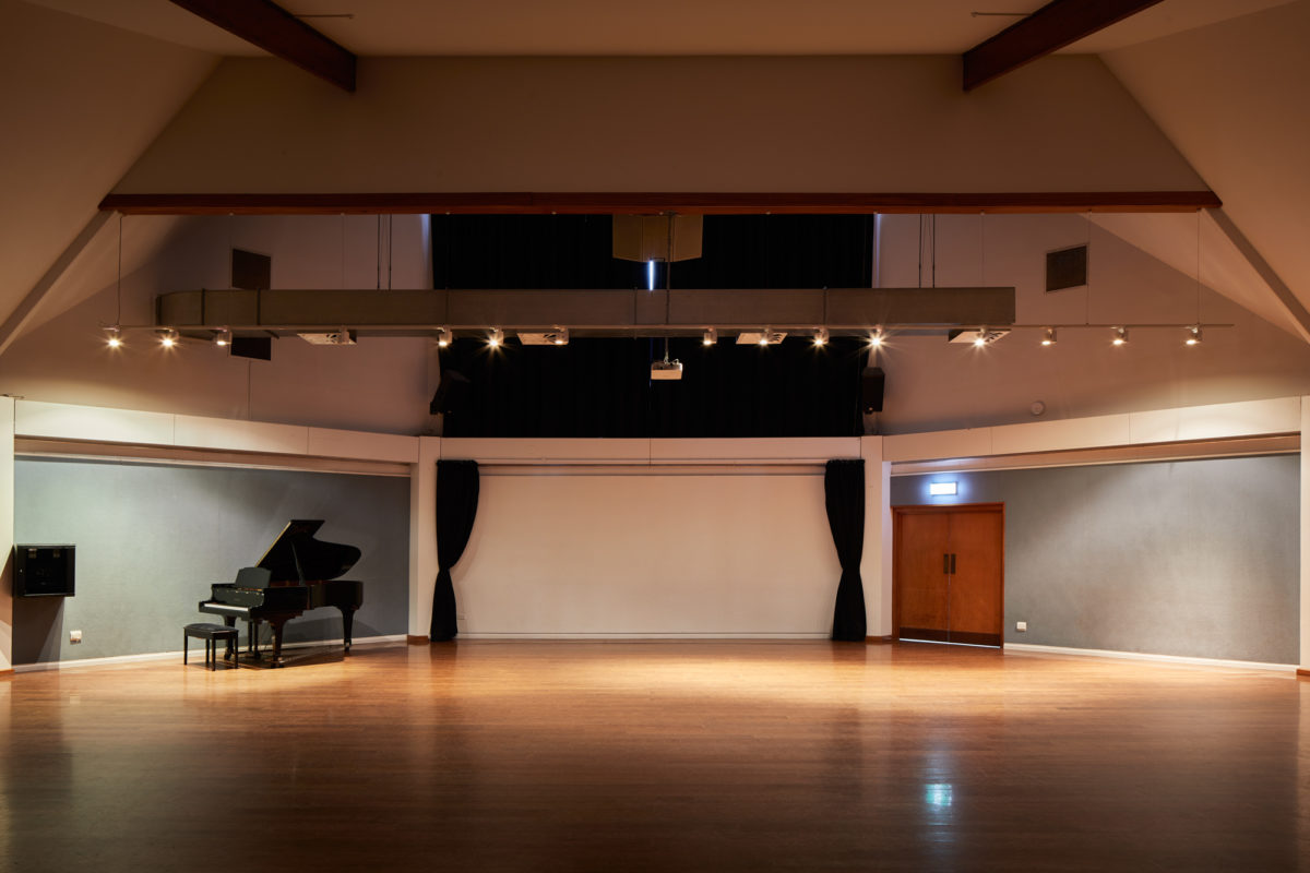Large performance hall with timber floor, track lighting rig, grand piano and dark curtain backdrop