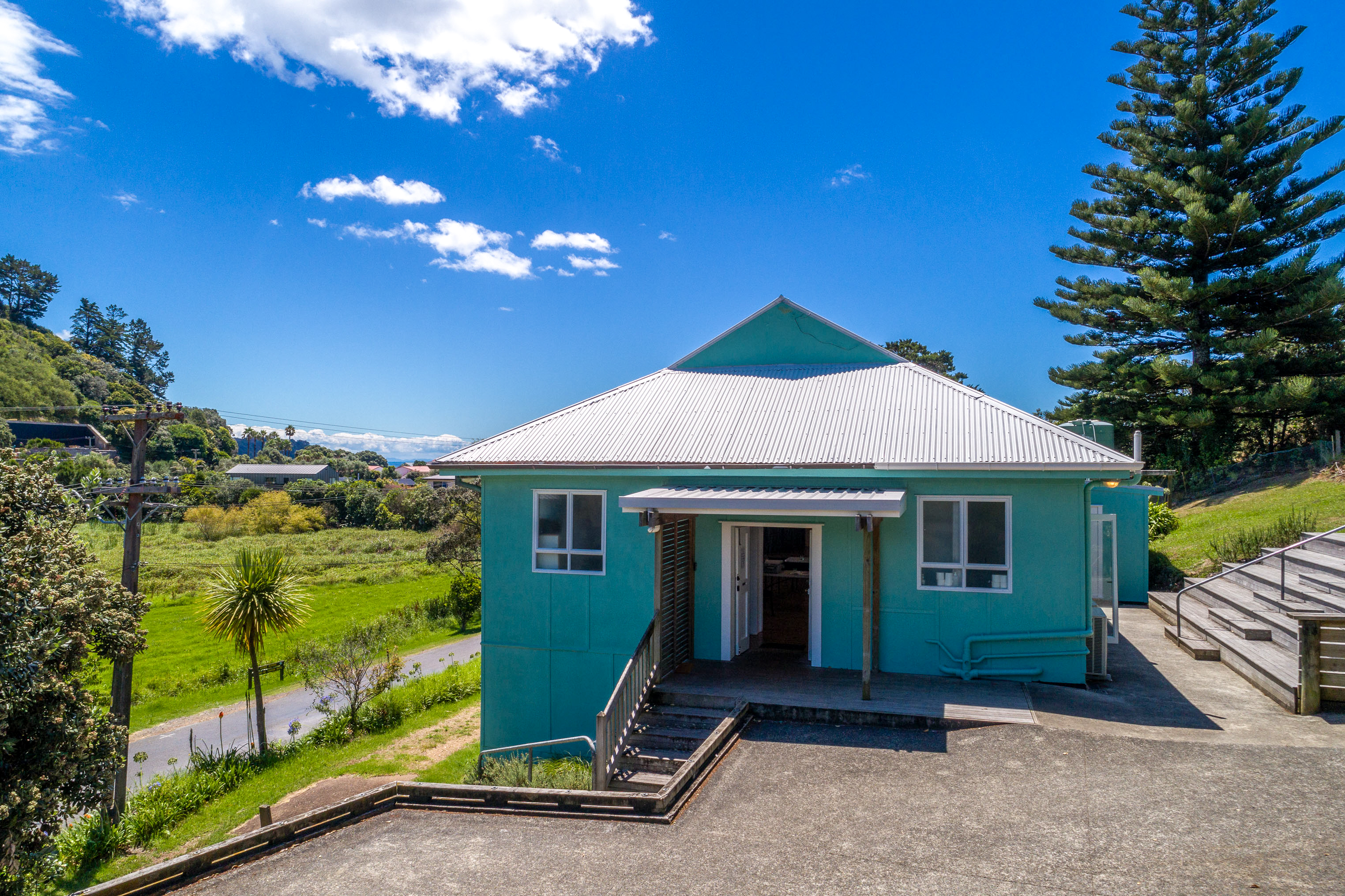 Aerial view of small teal-painted hall with corrugated iron roof on grassy site