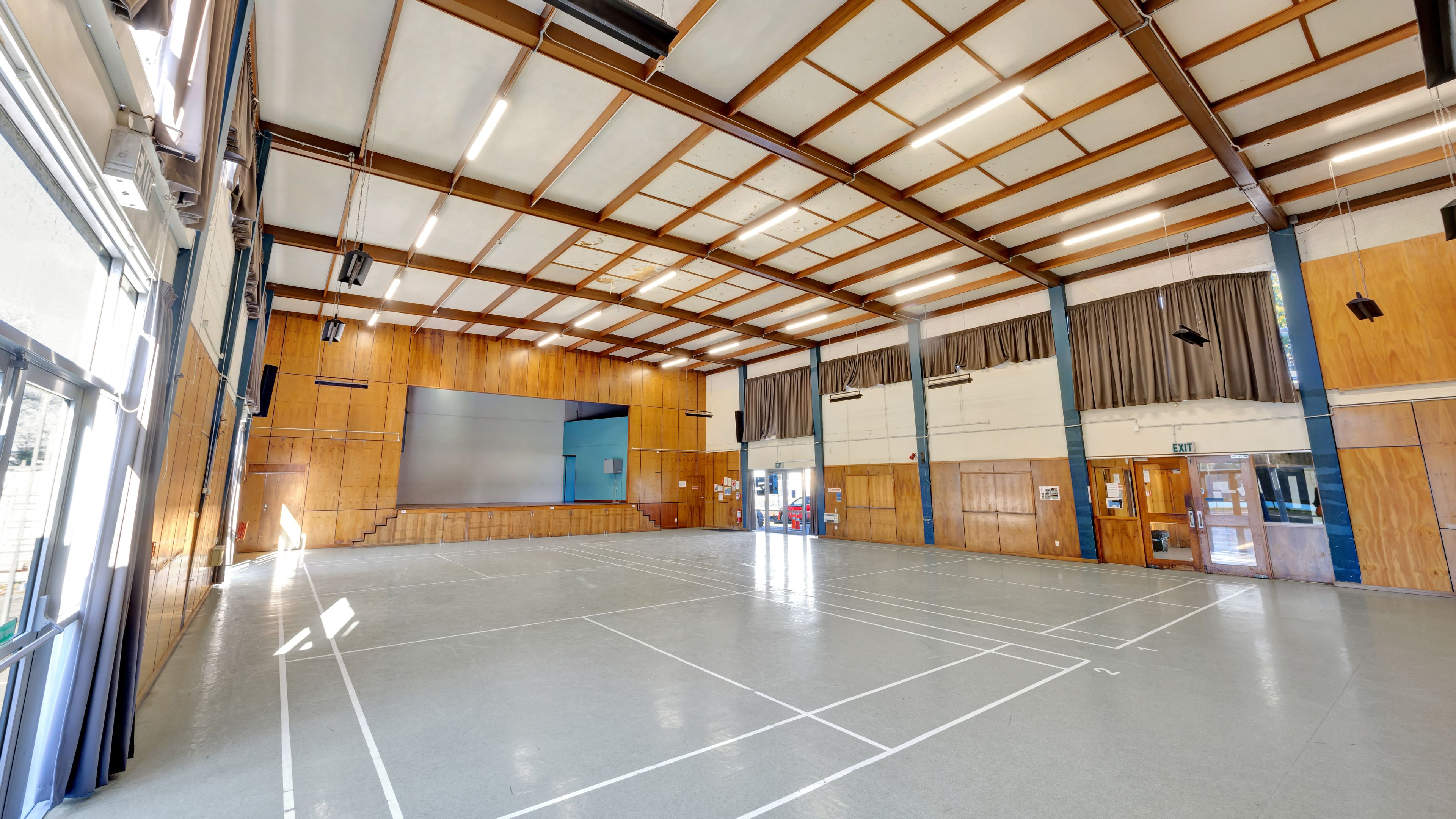 Large open hall with polished concrete floor, timber-panelled walls, high ceiling with steel trusses and projection screen