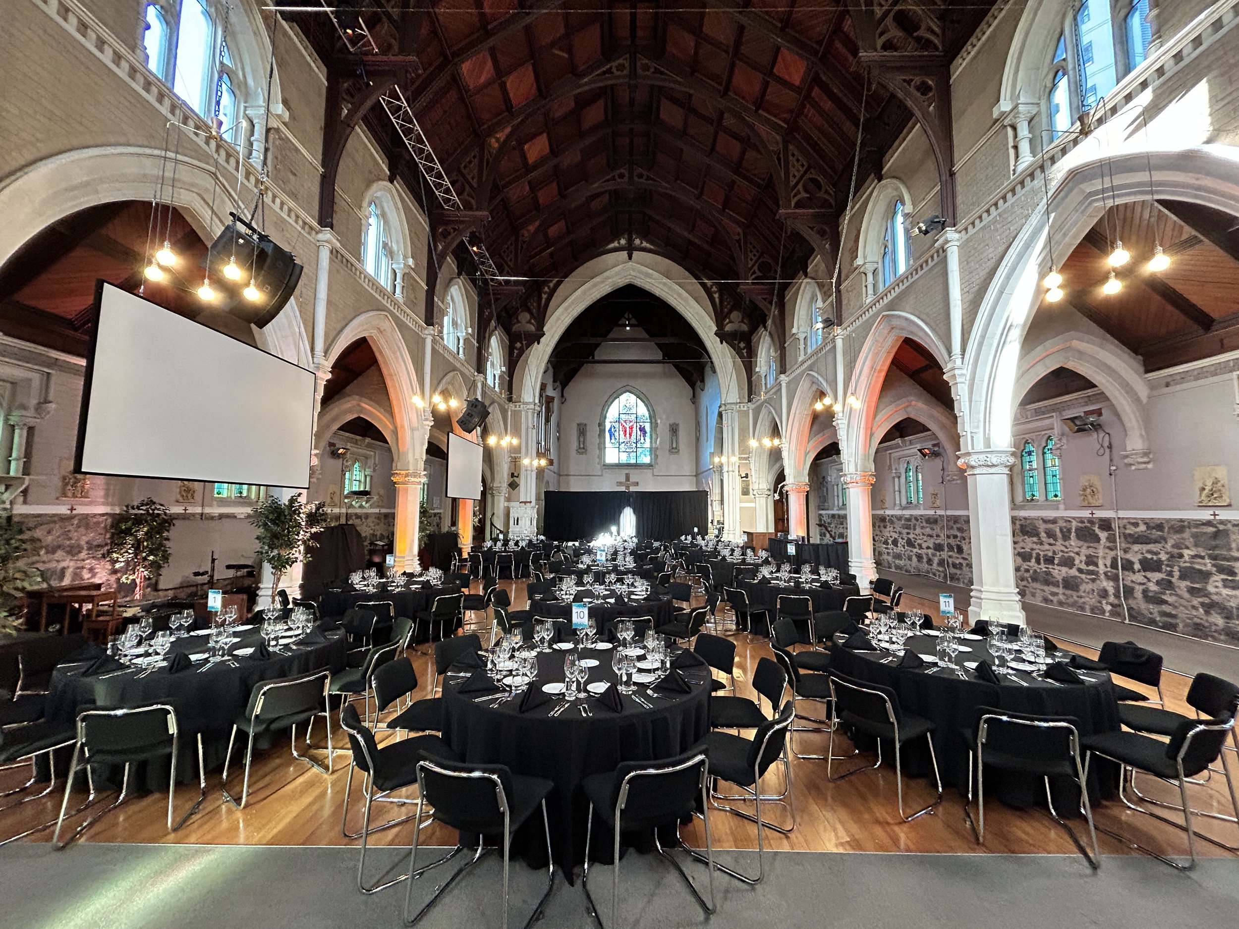Gothic church interior set with black-draped round banquet tables, stained glass windows, and timber nave
