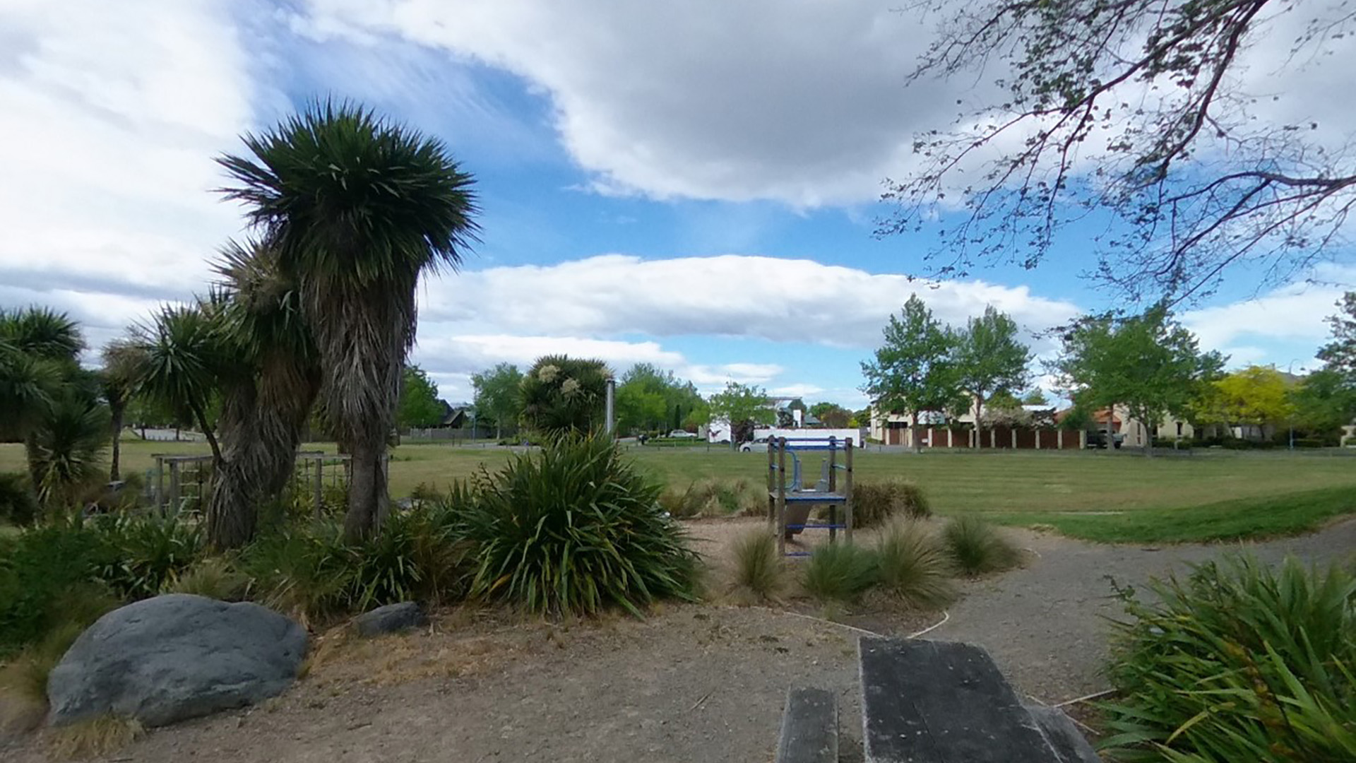 Open park area with native plantings, grass, and small play structure