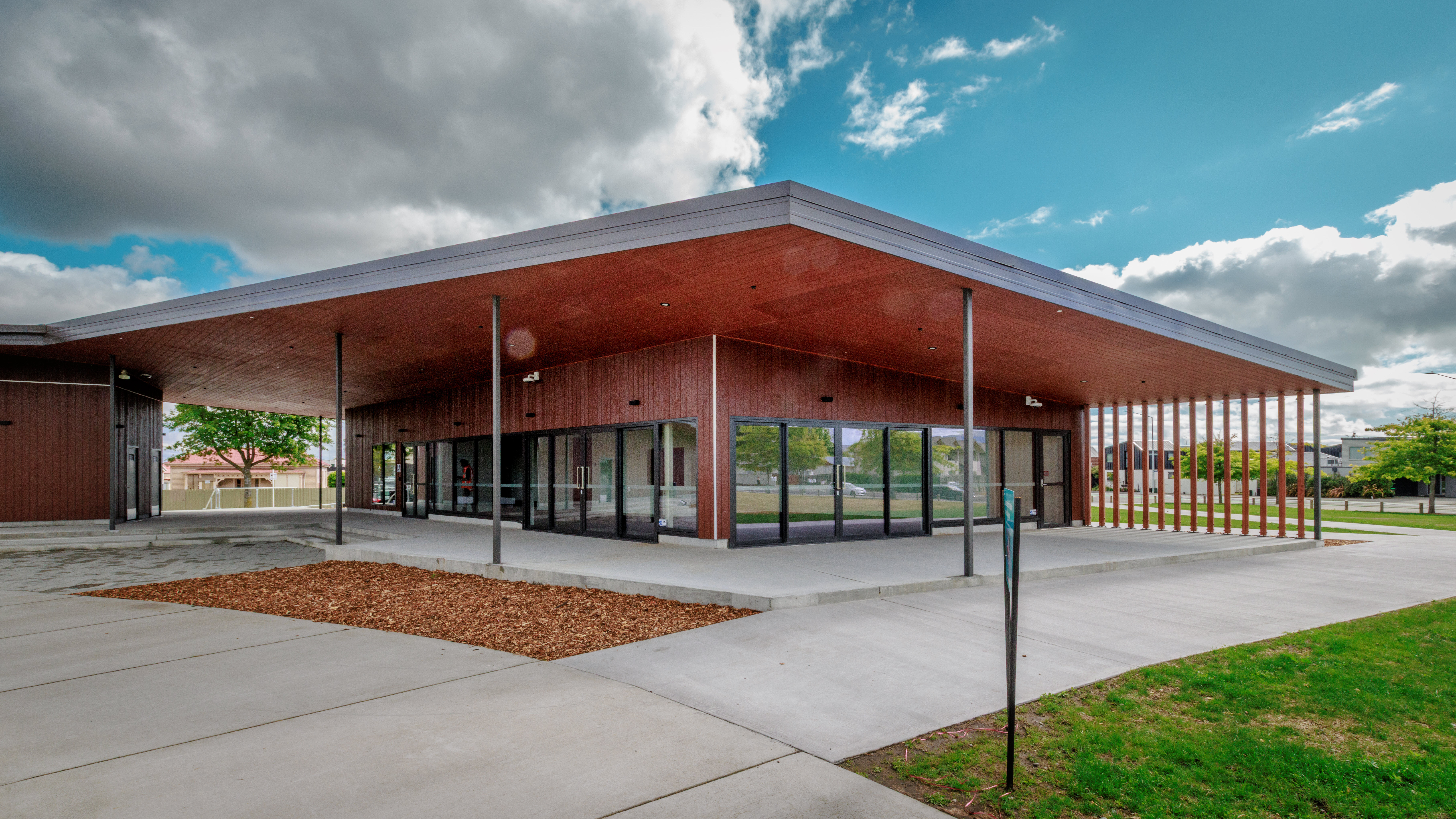 Low flat-roofed timber building with a wide canopy, glass frontage, and paved surrounds on open grounds