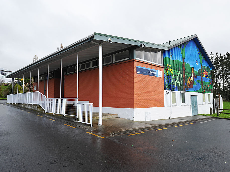 Red brick hall with covered verandah, white railings, and a large painted mural on the gable end