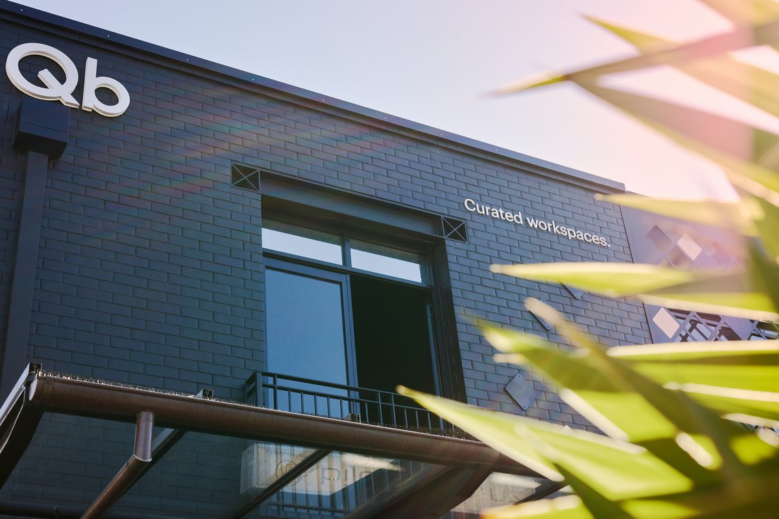 Dark brick building facade with Qb logo and curated workspaces text, viewed from below