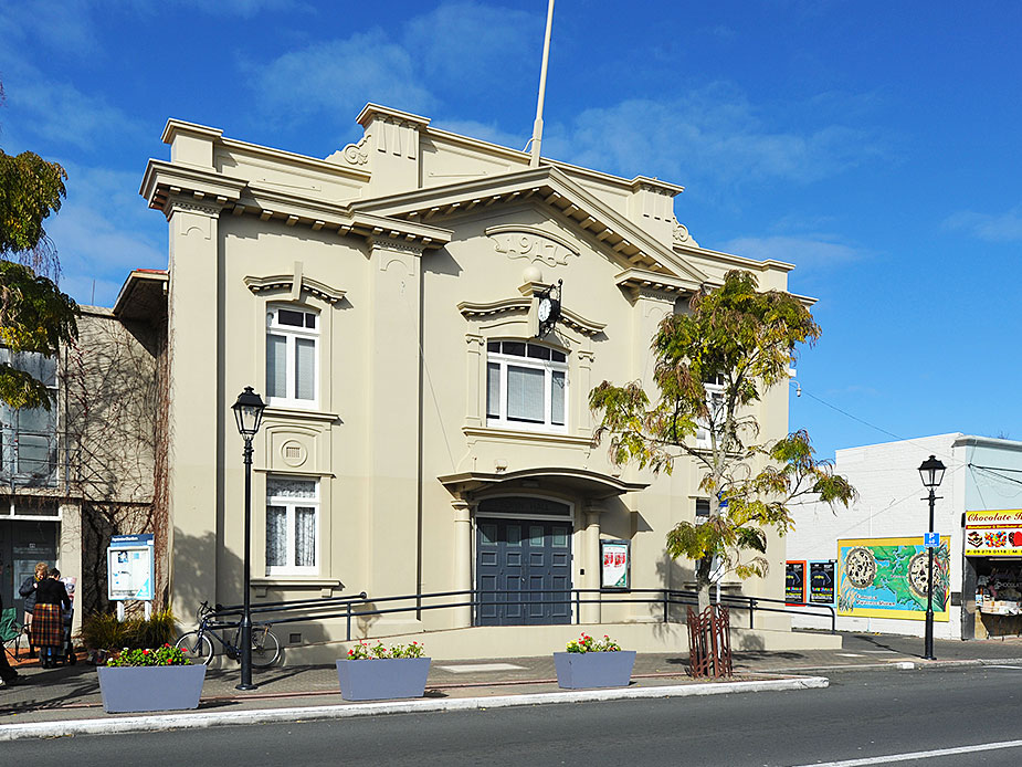Cream rendered heritage hall with ornate parapet, double doors and street-level planter boxes