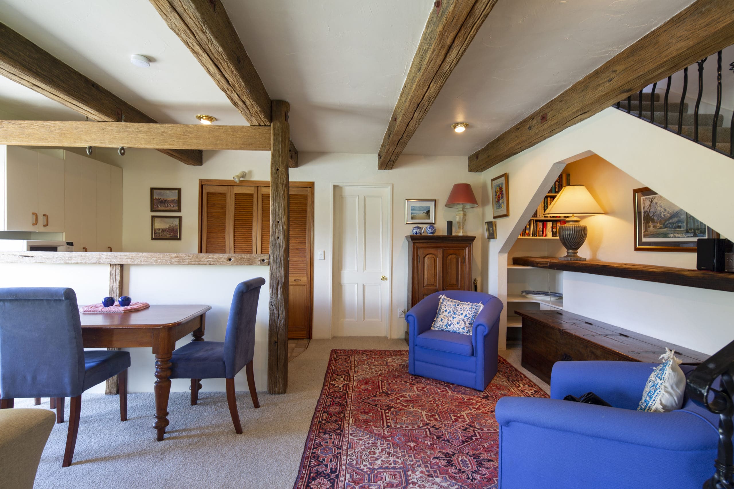 Cottage interior with exposed timber beams, a dining table and sitting area looking to the garden