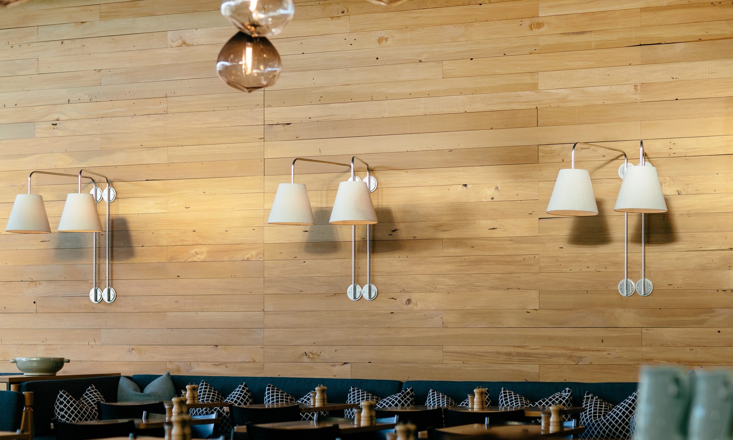 Restaurant wall with timber cladding and wall-mounted lamps above banquette seating