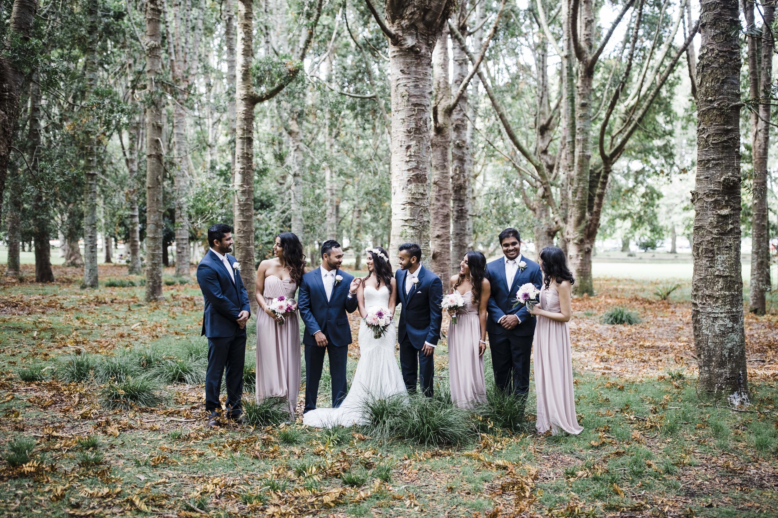 Wedding party among silver birch trees on a lawn scattered with autumn leaves