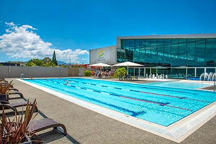 Outdoor swimming pool with lane markings and glass-fronted building behind