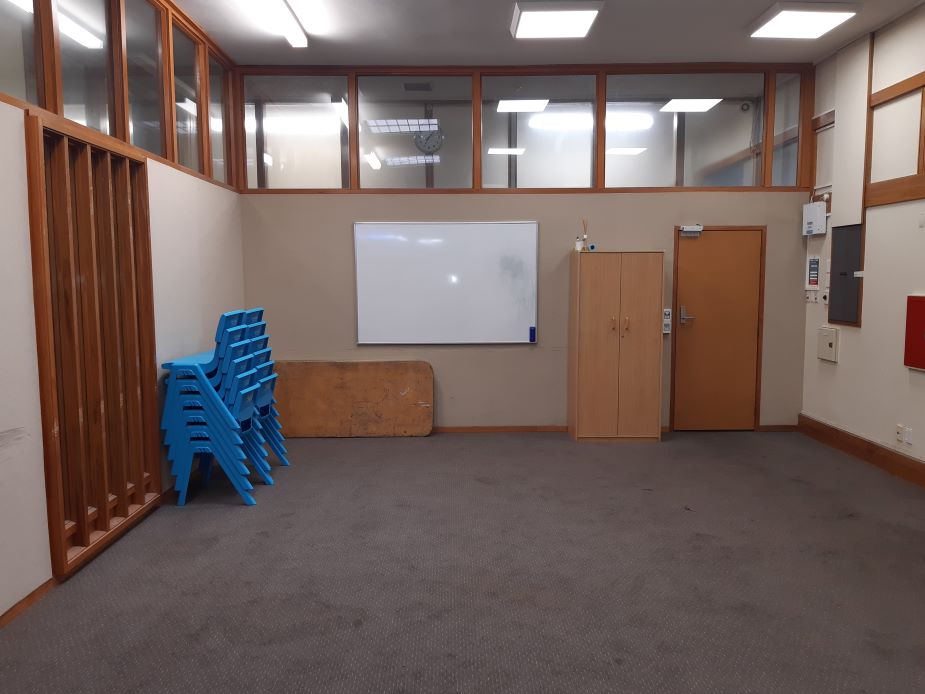 Empty carpeted room with stacked blue chairs, whiteboard and high windows