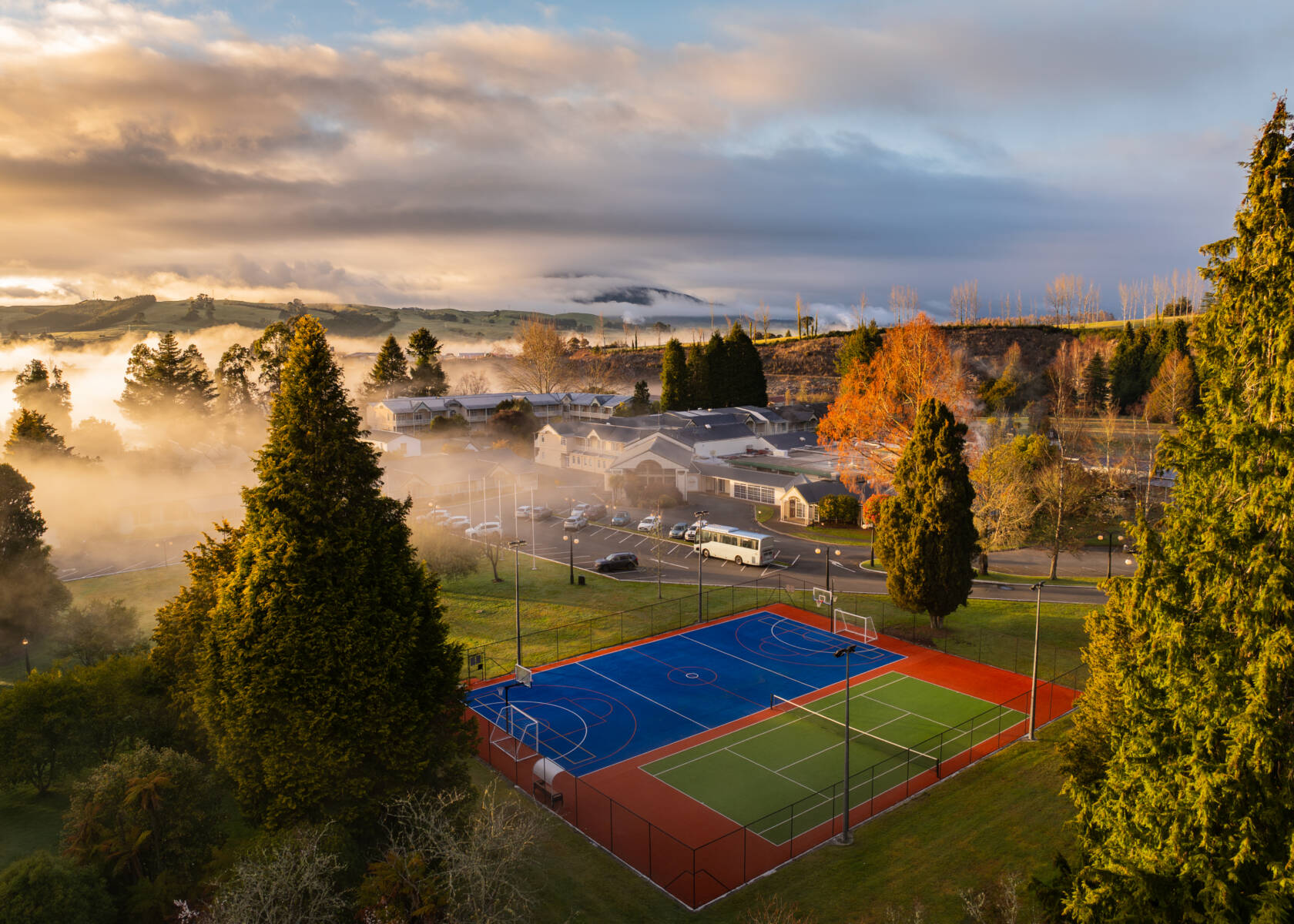 Aerial view of resort grounds with sports courts, trees, and misty hills beyond