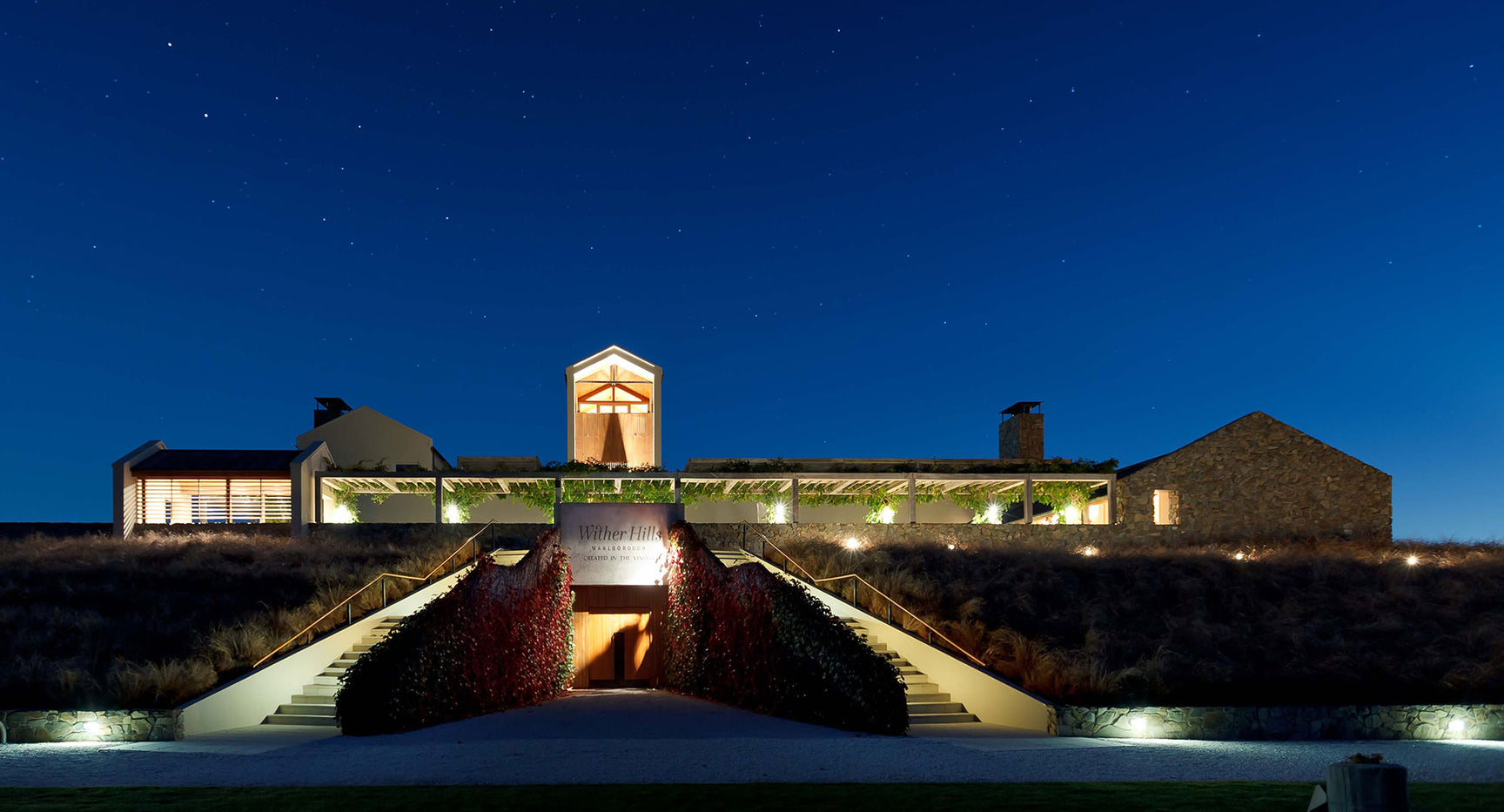 Illuminated winery buildings at dusk with landscaped grounds