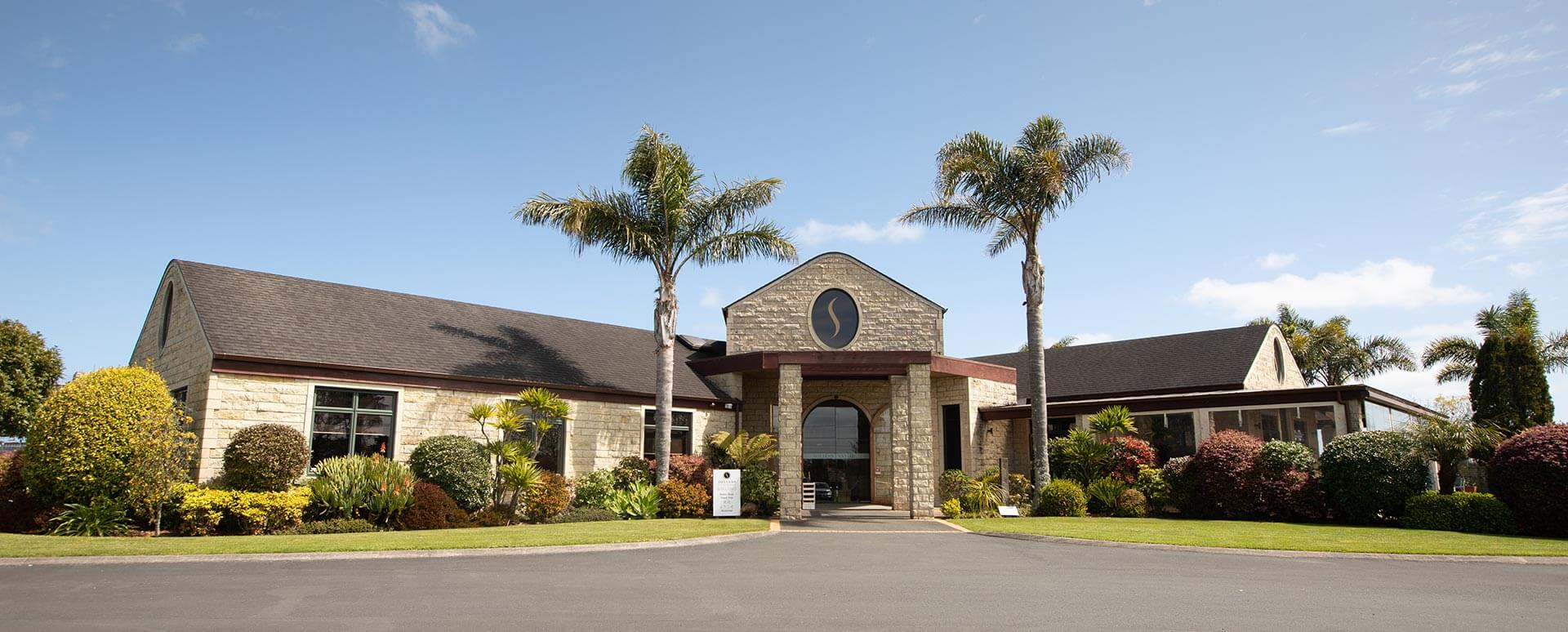 Stone and timber winery building with palm trees and formal driveway