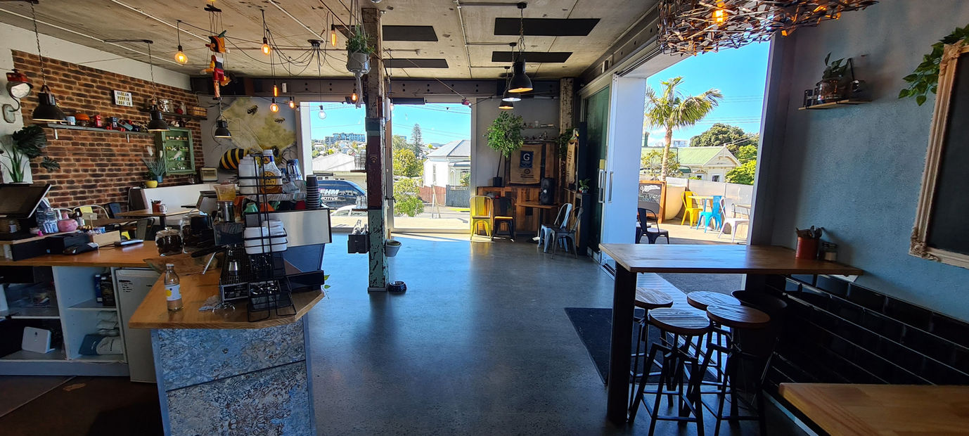 Cafe interior from entrance showing counter, open roller door, and outdoor area