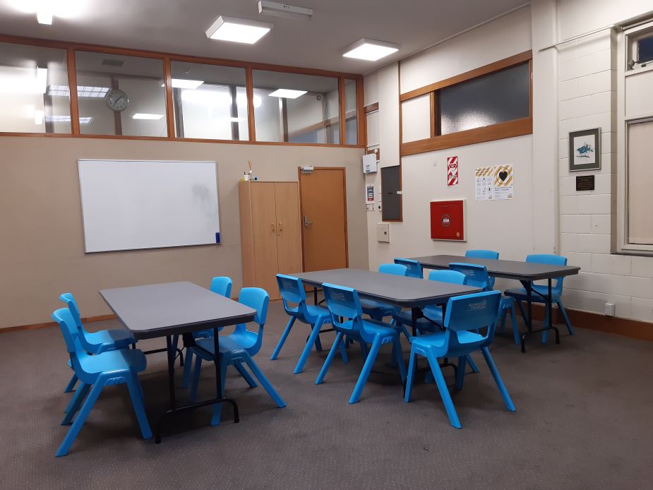 Carpeted room with blue chairs and tables arranged for classroom use
