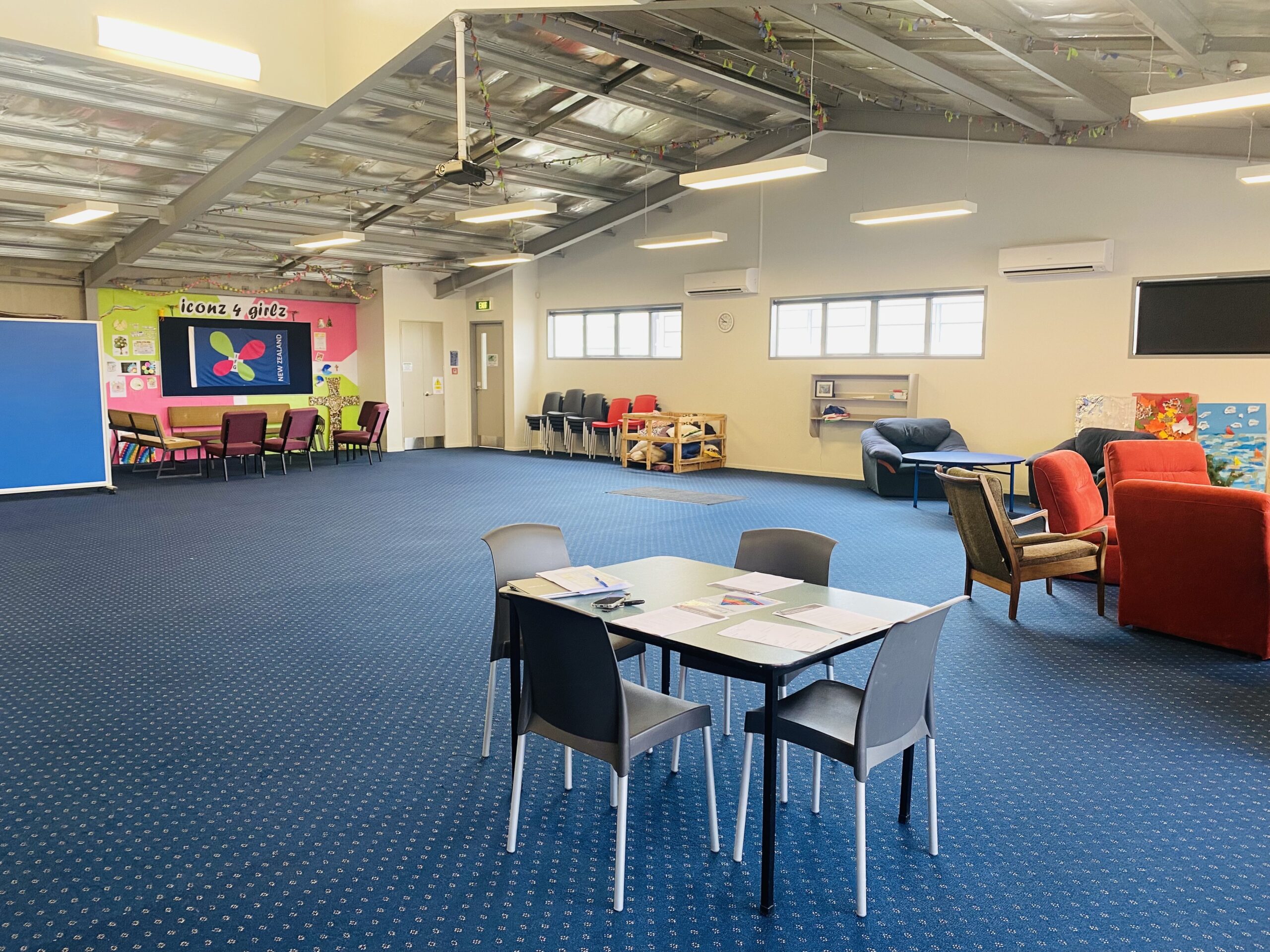 Large open room with blue carpet, tables, chairs, and colourful wall mural
