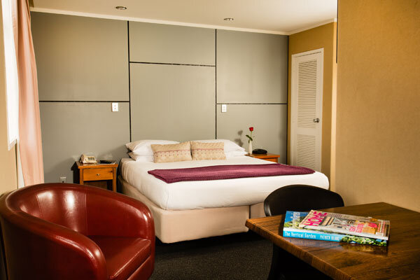 Hotel room with upholstered bed, armchair and timber side table