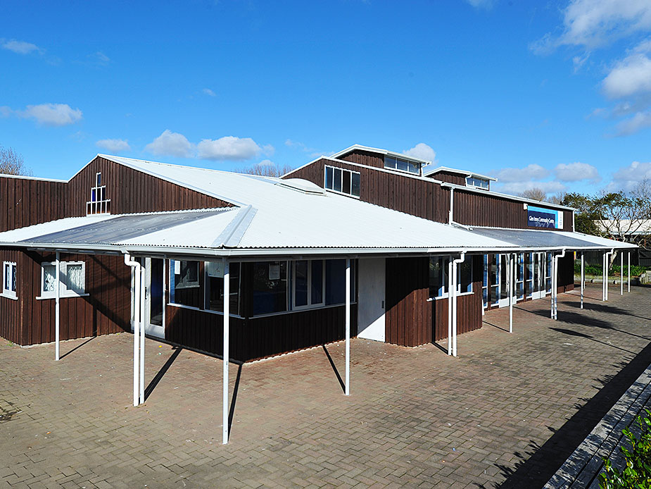 Dark brown community centre building with covered entrance and brick paving