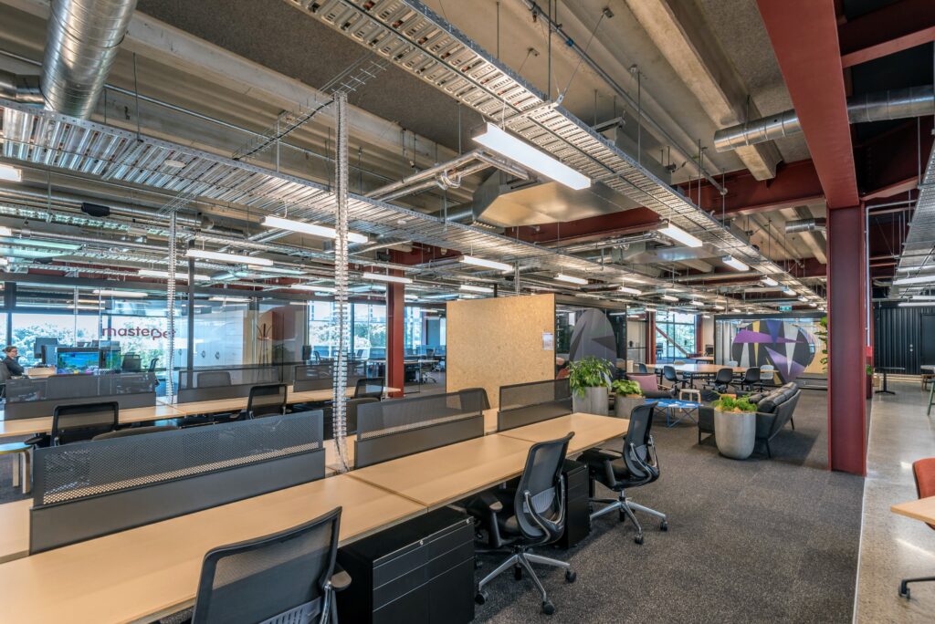 Open-plan co-working space with bench desks, exposed ducting, and red structural columns