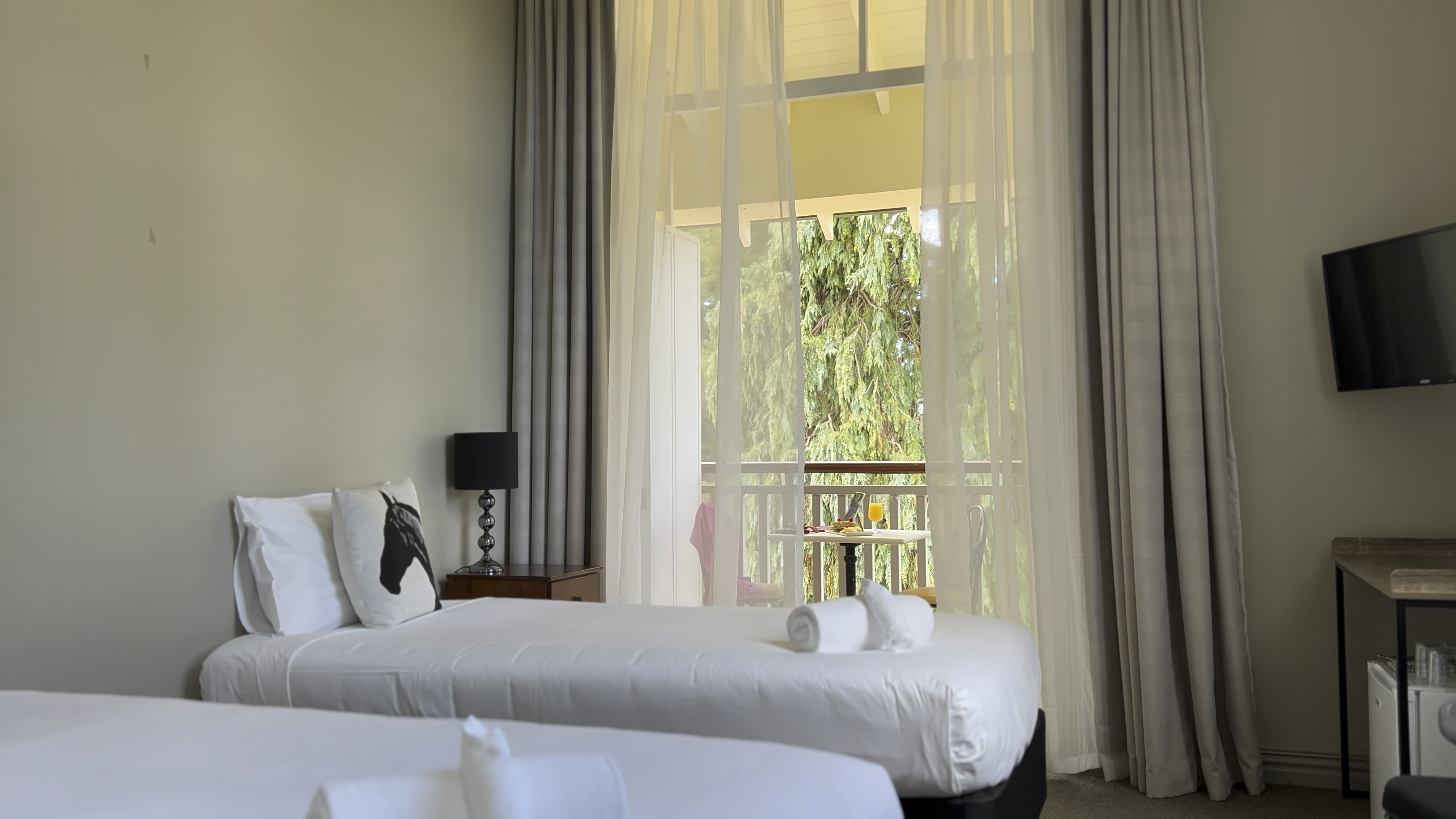 Hotel room with twin beds, sheer floor-to-ceiling curtains, balcony overlooking trees