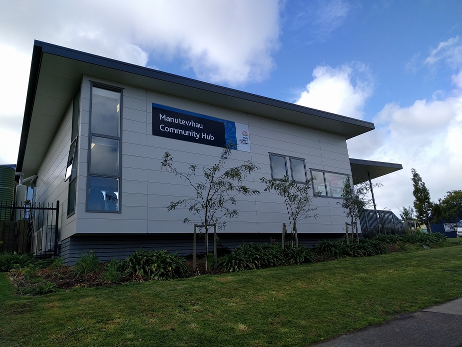 Single-storey community hub building with flat roof, signage board, and garden border