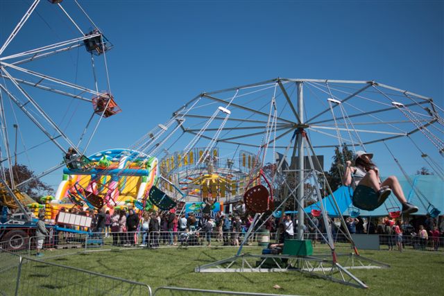 Fairground rides and crowds on open grass at outdoor show event