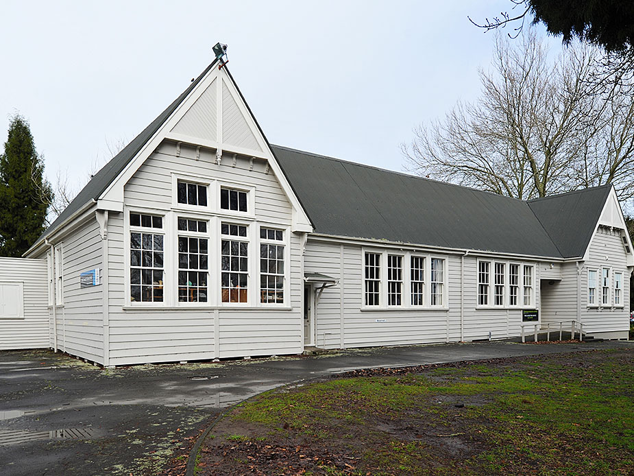 White weatherboard hall exterior from driveway angle with trees