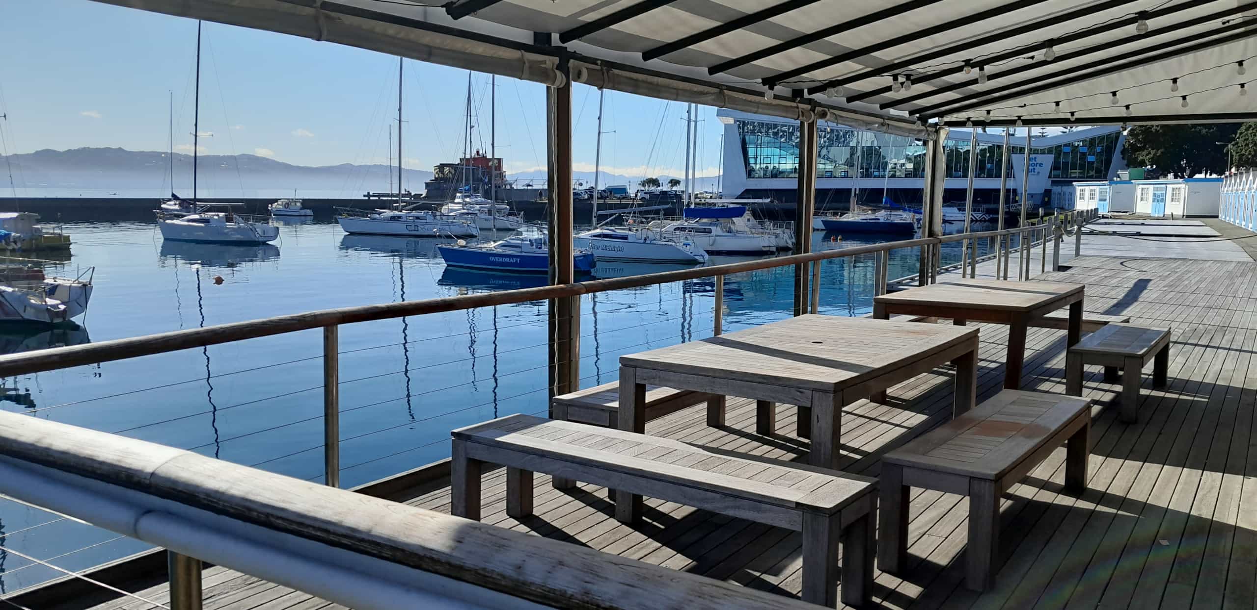 Timber deck overlooking a marina with long timber benches, boats moored at calm waterfront