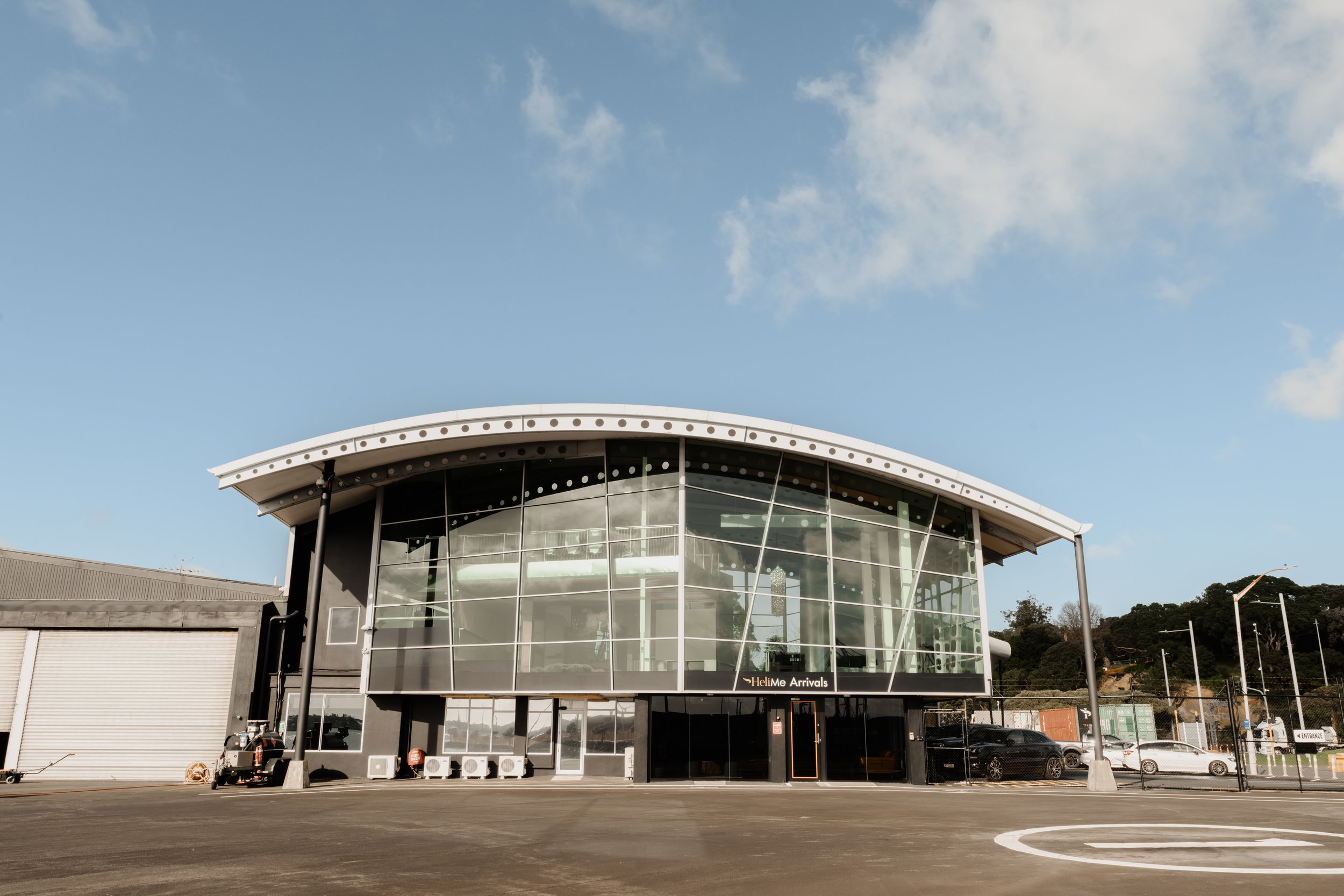 Curved glass and steel waterfront building with helipad markings in foreground