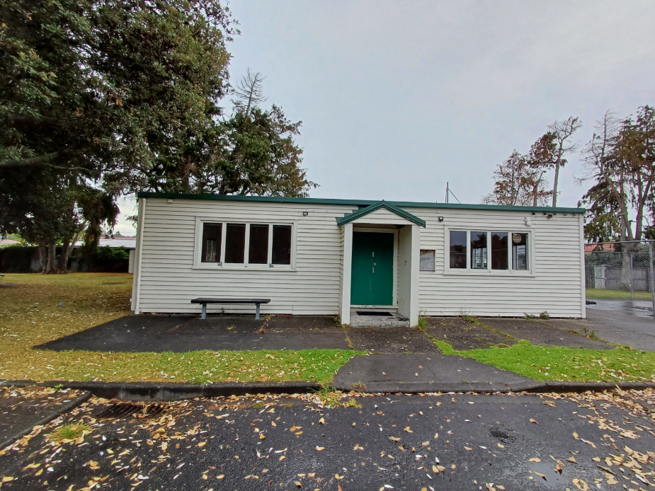 Small white weatherboard hall with green roof and entry door