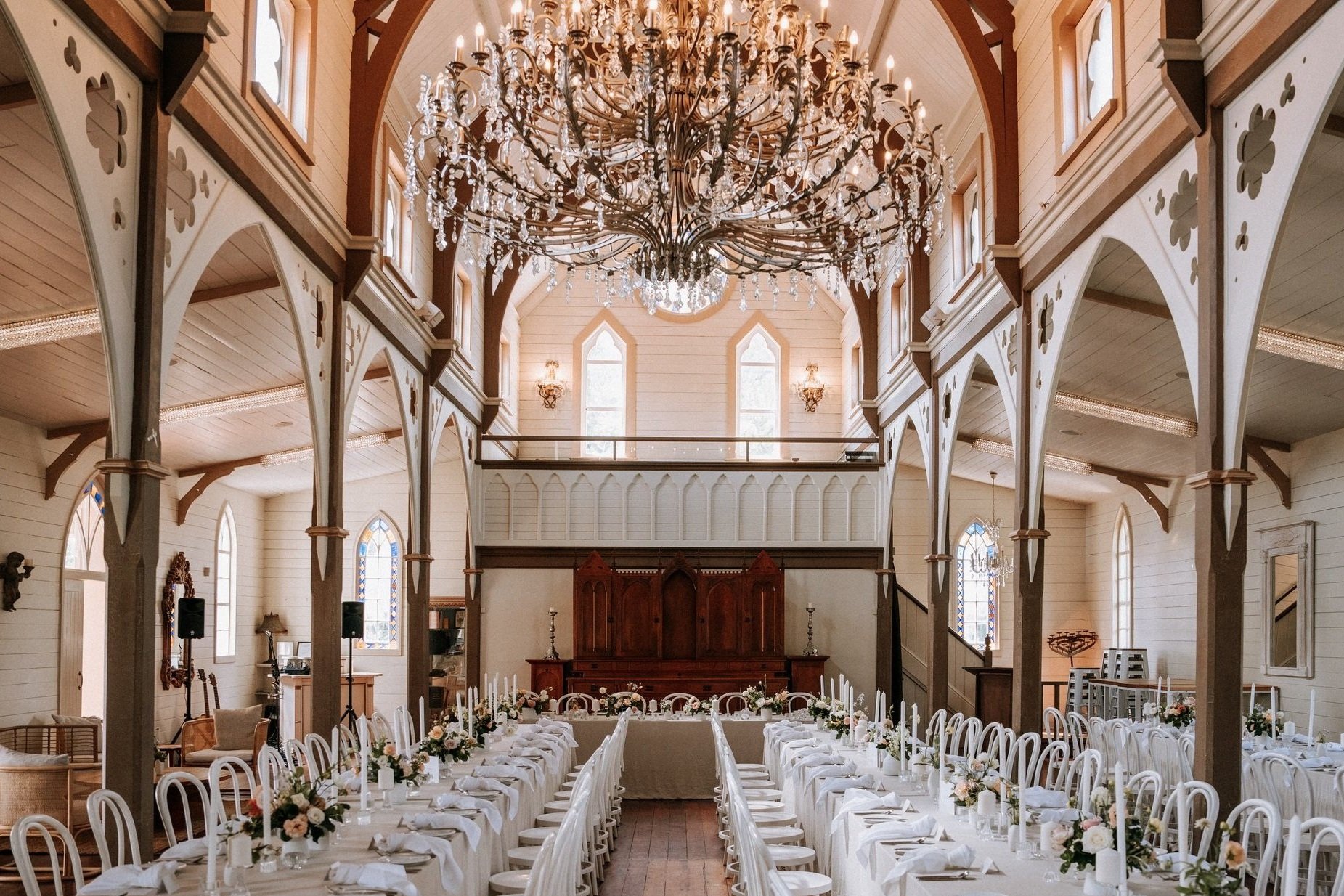 White timber church interior with arched nave, large chandelier and long tables set for dining