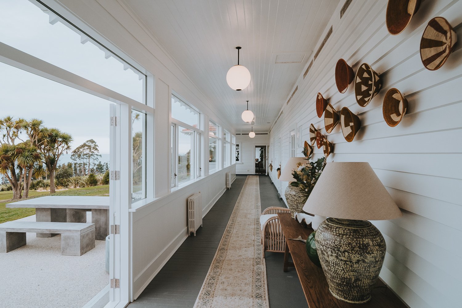 White-painted hallway with pendant lights, woven wall hangings and view to outdoor seating