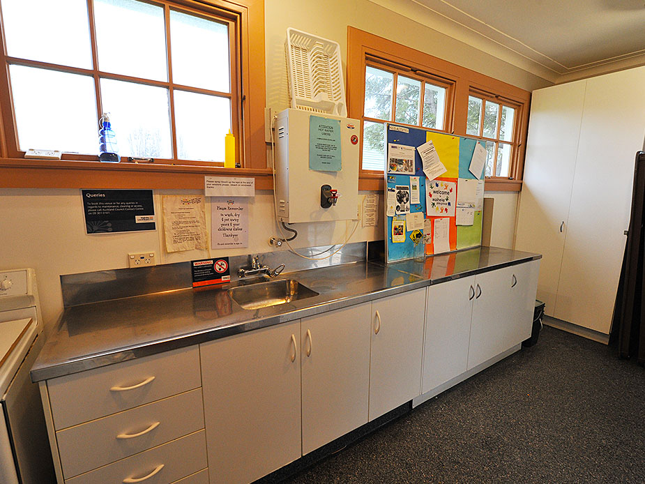 Basic hall kitchen with stainless steel bench, white cabinets, and notices on wall