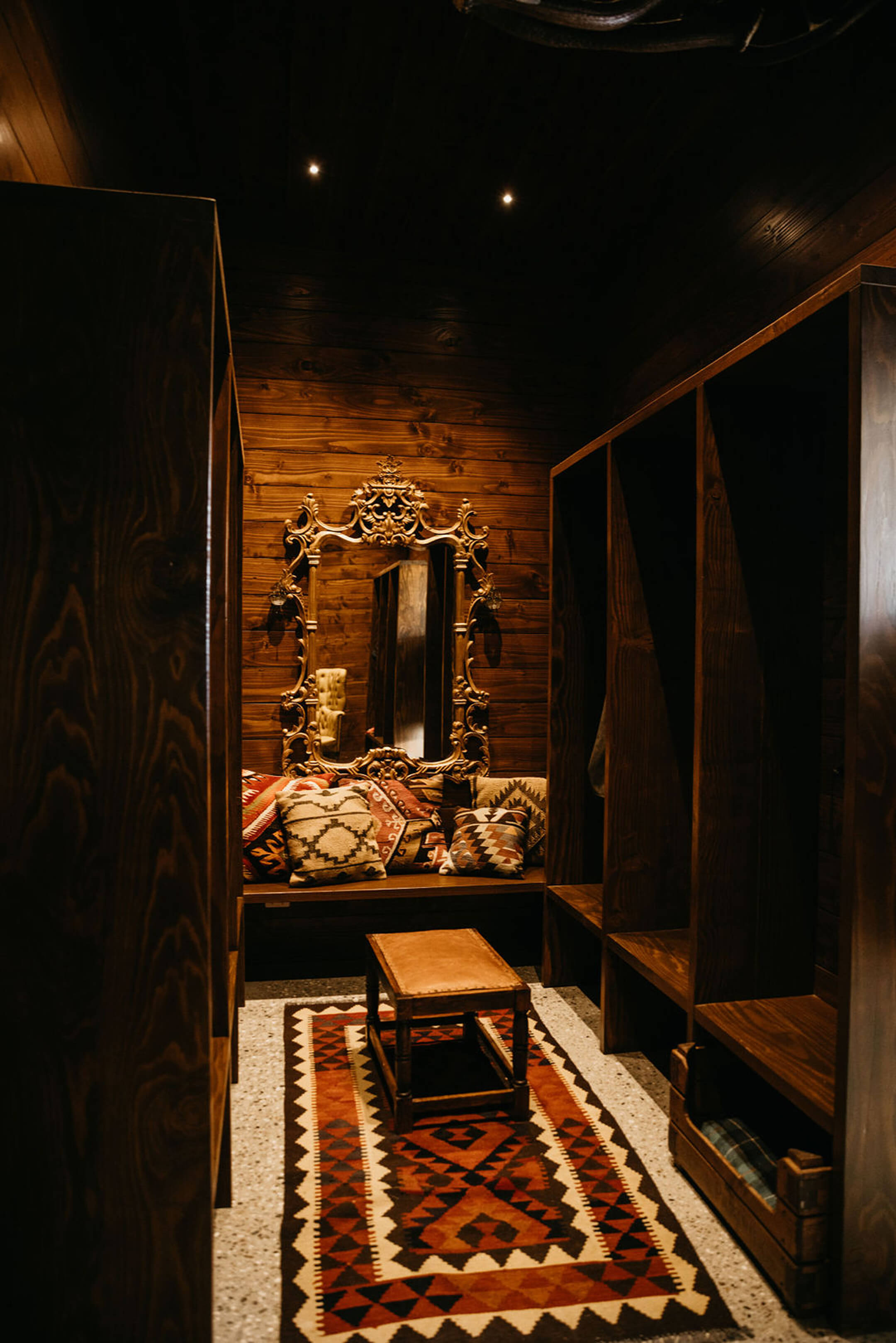 Dark timber-panelled lounge nook with a gilt mirror, kilim rug and built-in bench seating