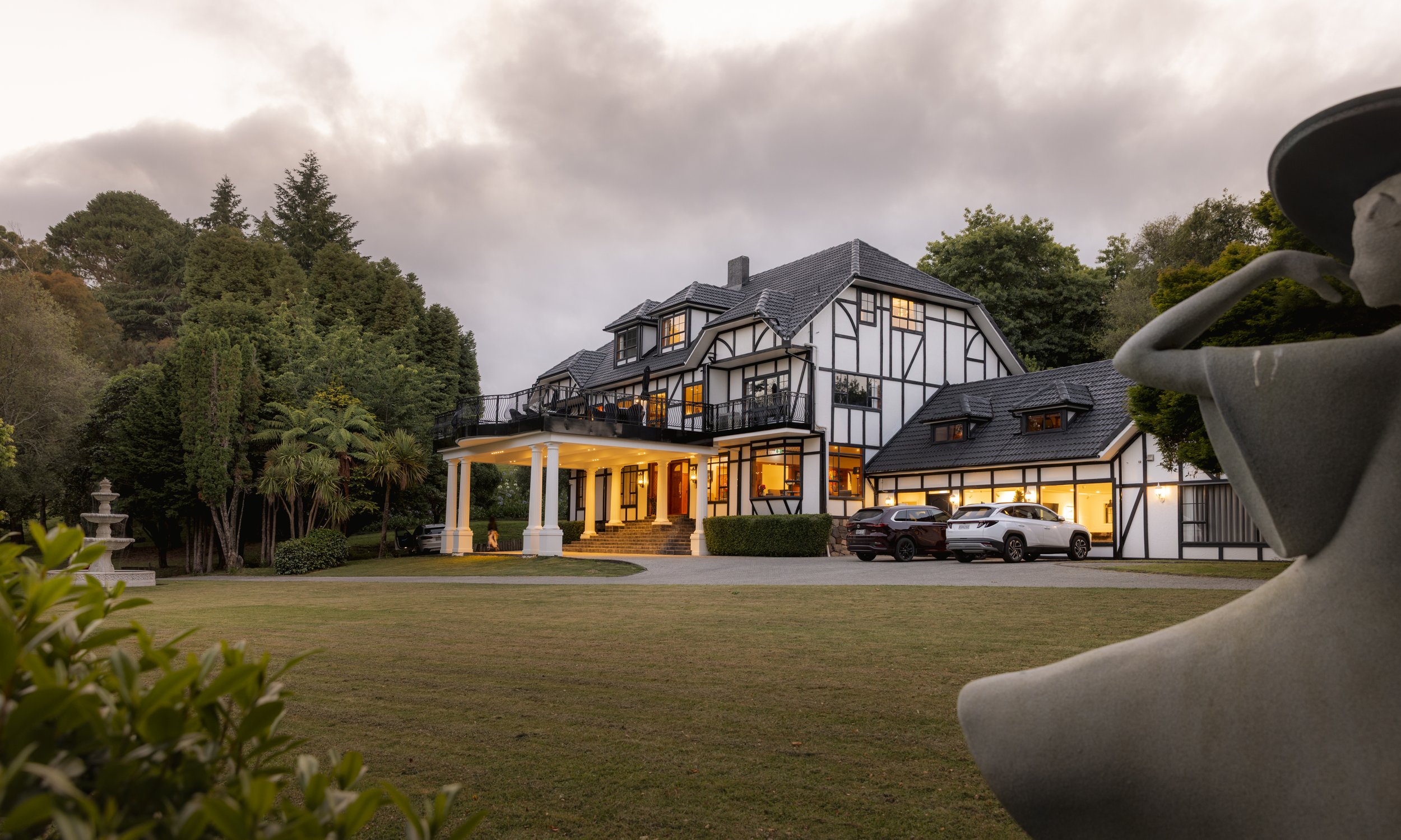 Large Tudor-style manor house with white and dark timber facade set on lawn at dusk