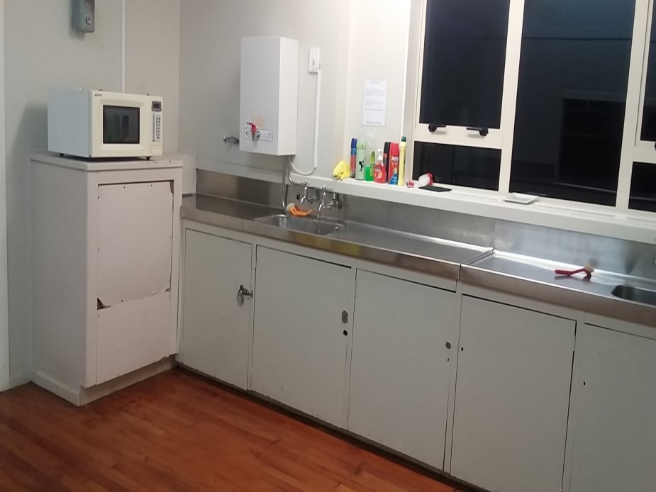 Basic kitchen with white cabinetry, stainless bench, sink and microwave on timber floor