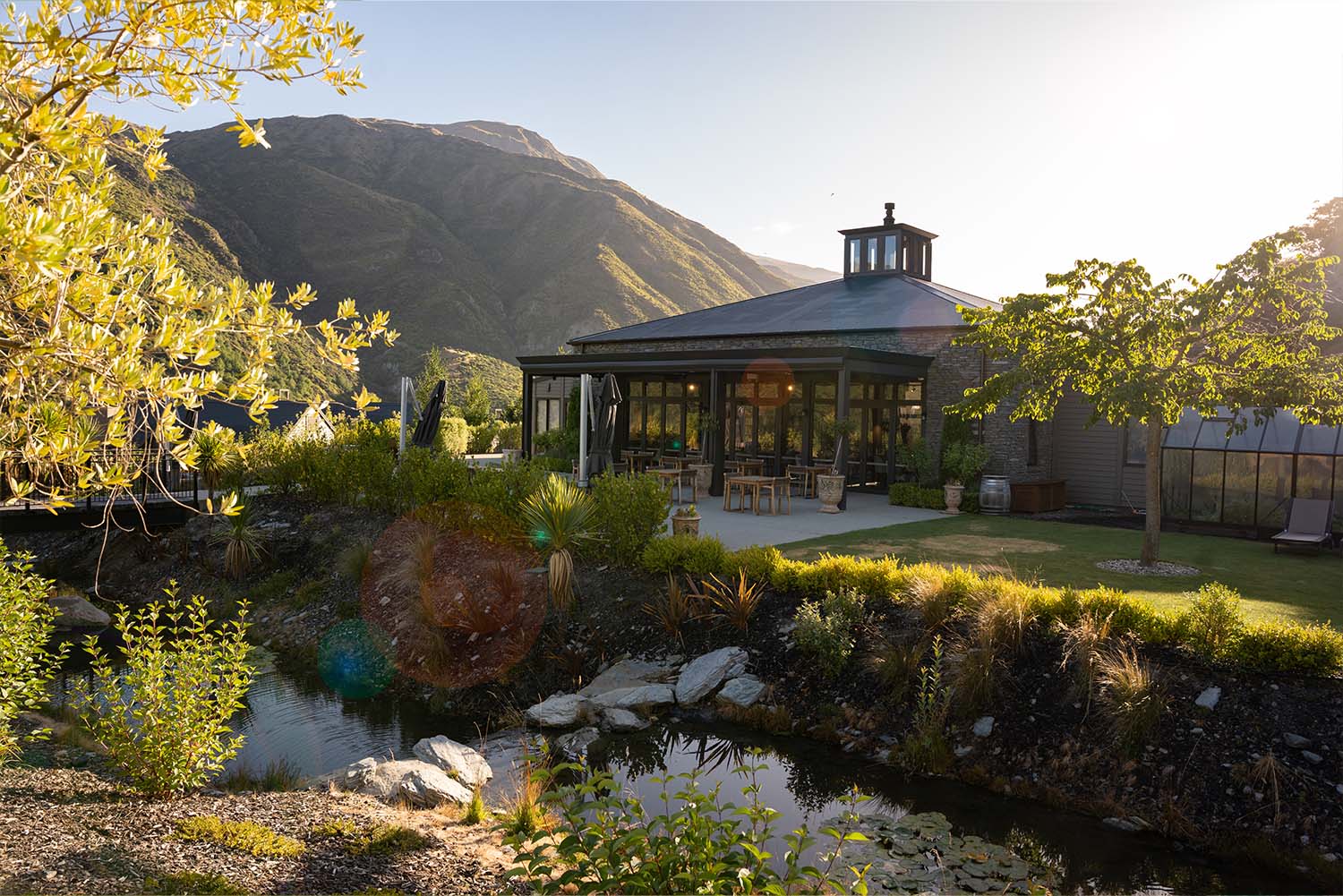 Pavilion building with pond, garden and mountain backdrop at sunset
