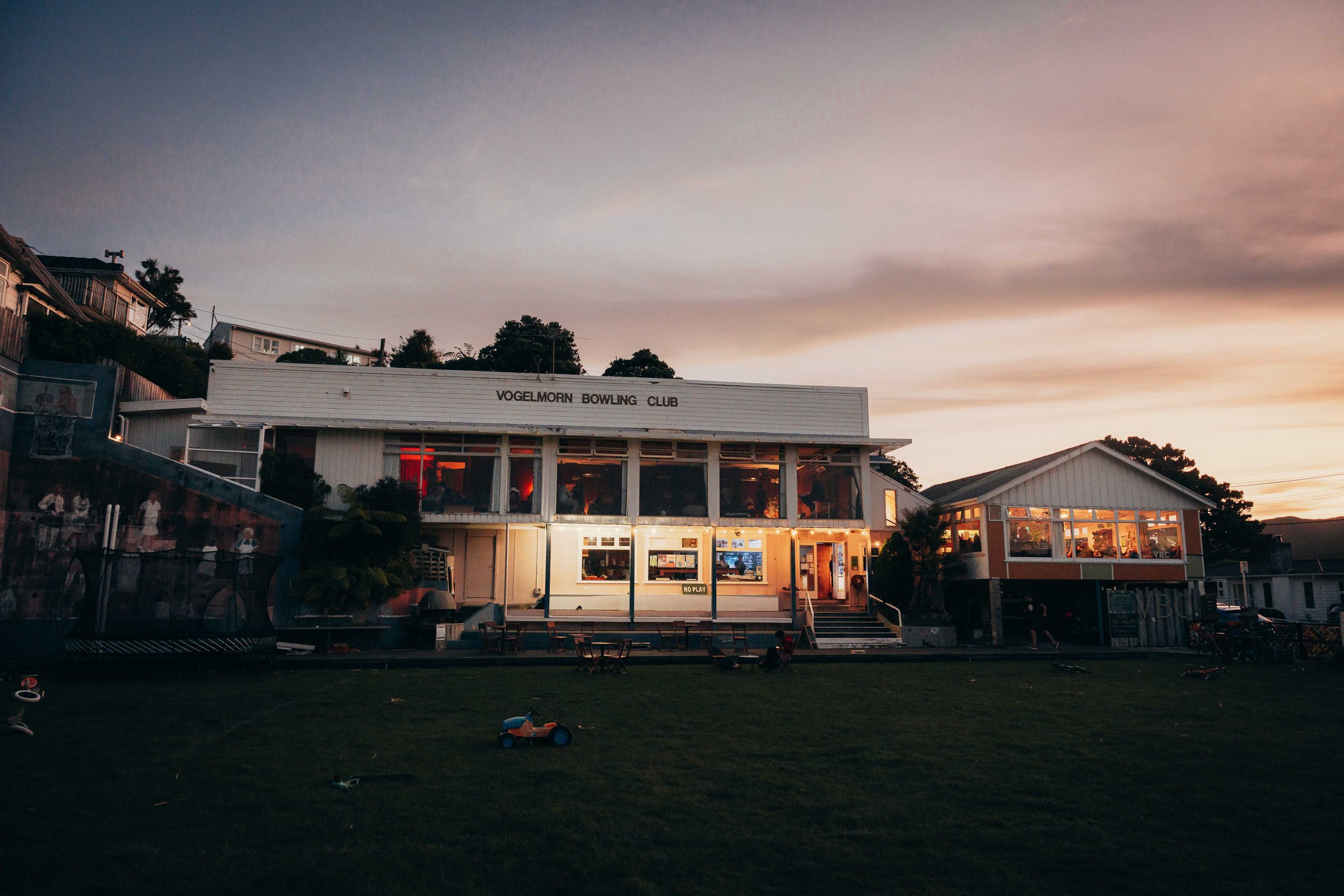 Vogelmorn Bowling Club building lit up at dusk with green lawn in foreground