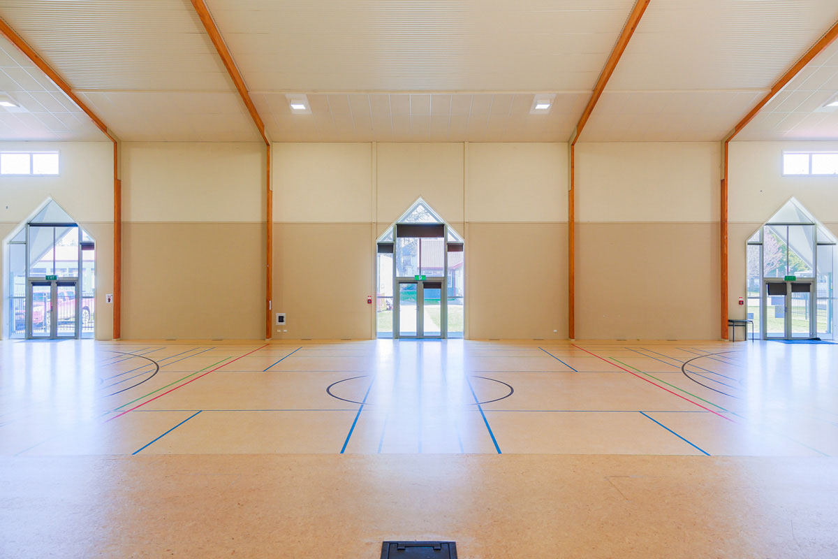 Large sports hall with multi-court timber floor, high ceiling, and three sets of folding doors